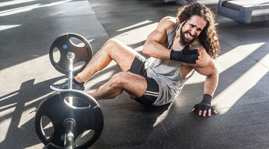 Injured bodybuilder working out with a barbell on the floor with a shoulder injury