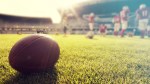 Close-Up Of Football Lying On Field Next To Football Players