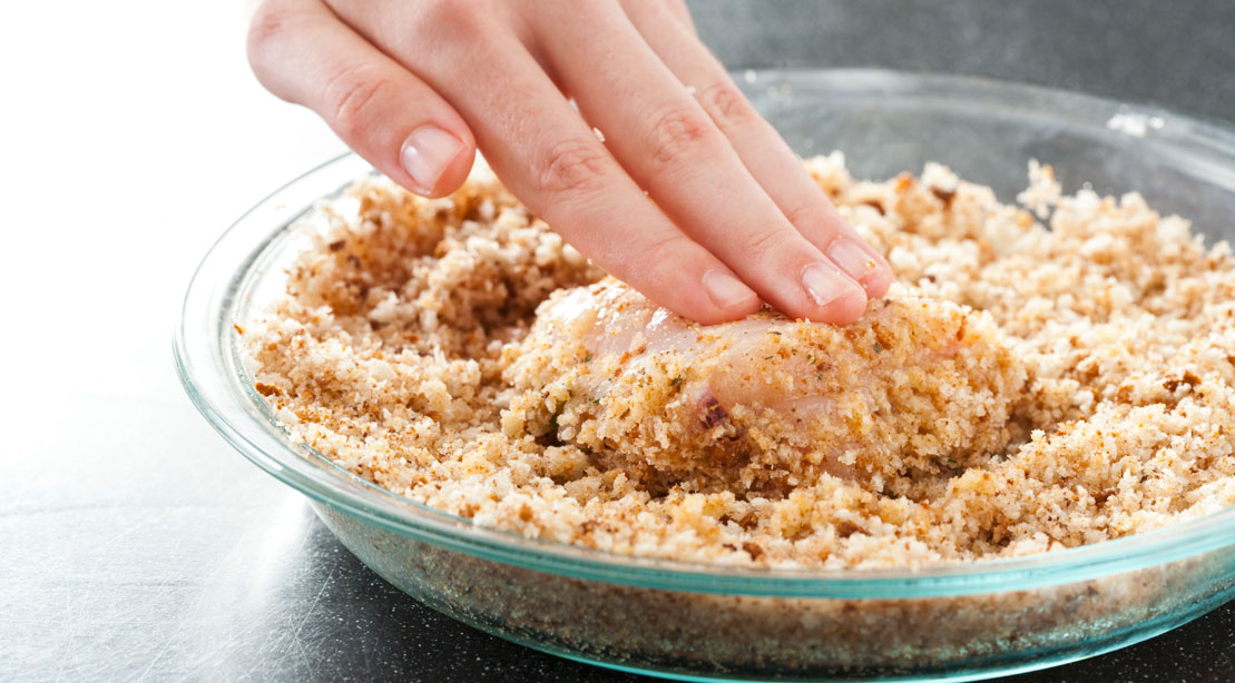 Hand crusting chicken breast in glass bowl