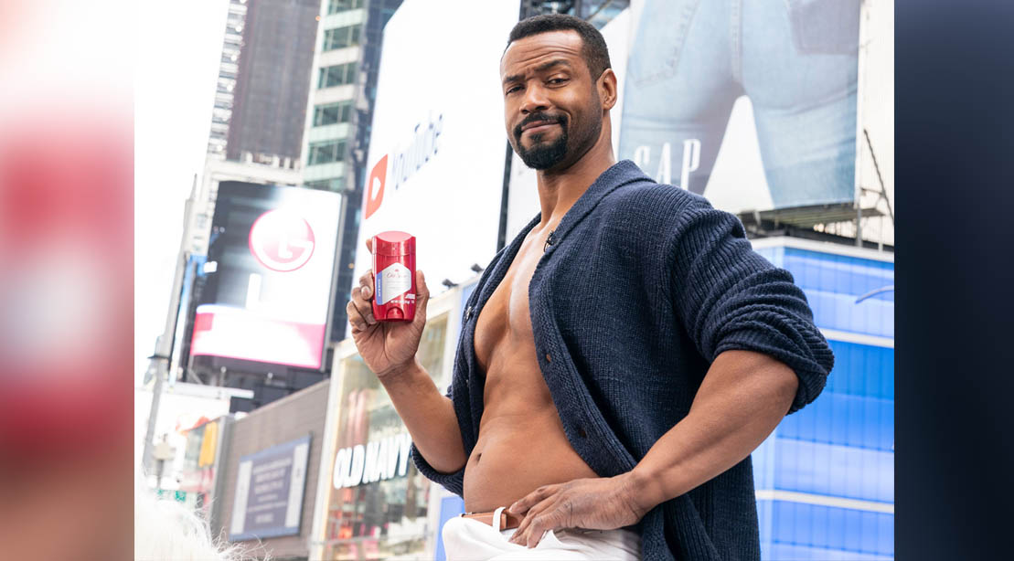 Old Spice commercial actor Iaiah Mustafa posing in times square with an old spice deodorant applicator