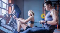 Young Man Exercising At Rowing Machine In Gym