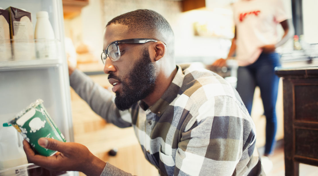 Man reading the nutrition label of a pint of ice cream in front of the fridge