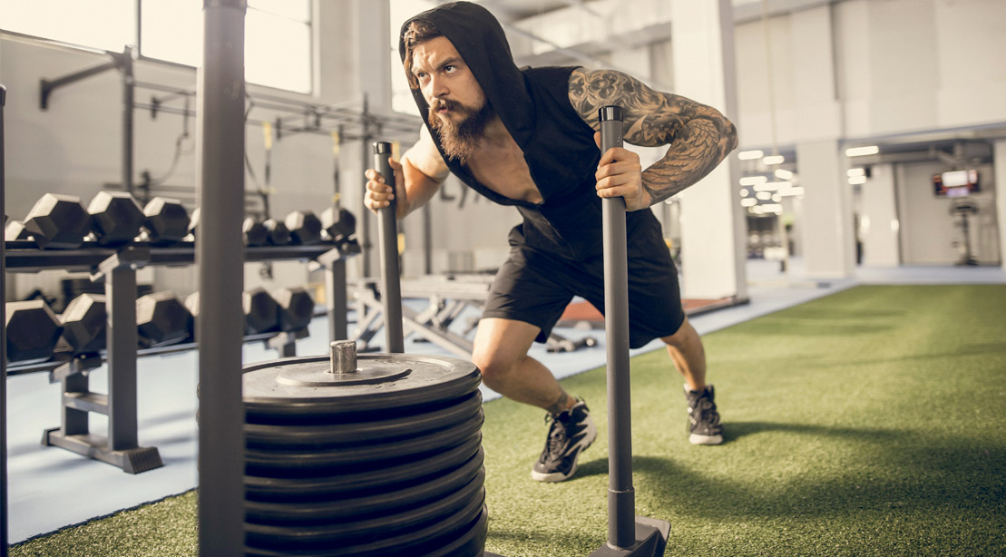 Focused fitness man working out with a sled push exercise in the gym