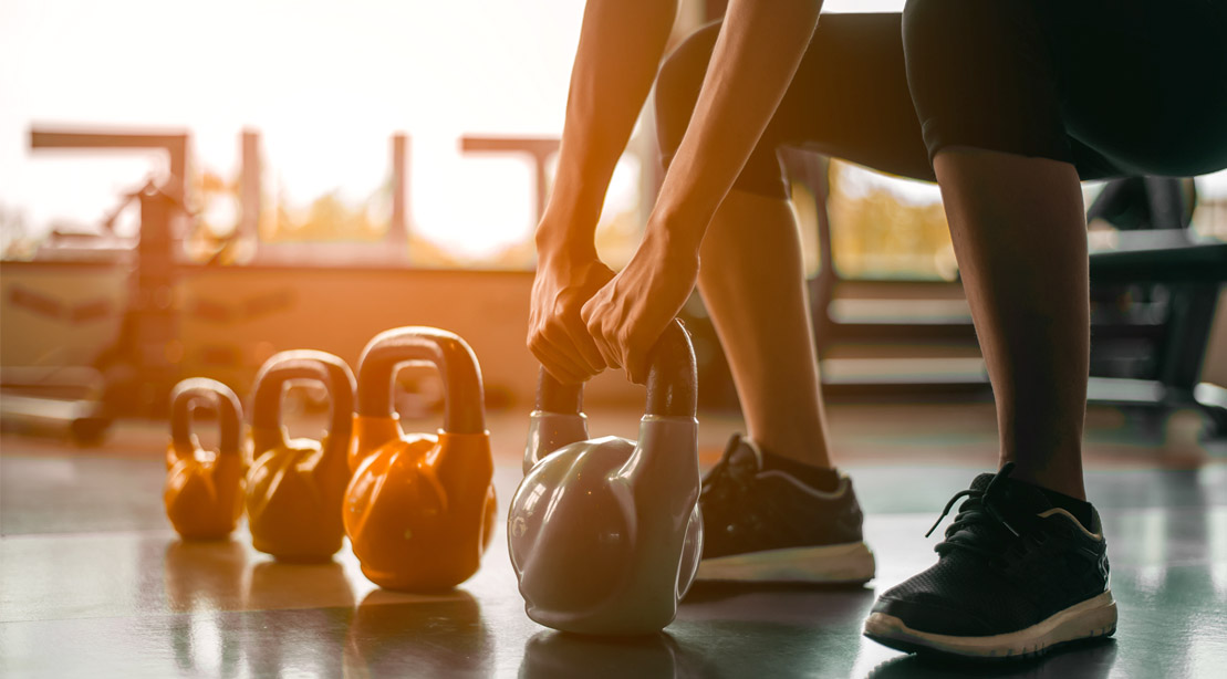 Fit female squating to lift a row of different size kettlebells