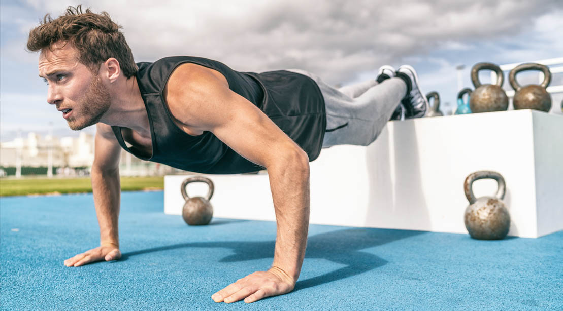 Fitness man working out outdoors doing an elevated feet pushup variation of a decline pushup exercise