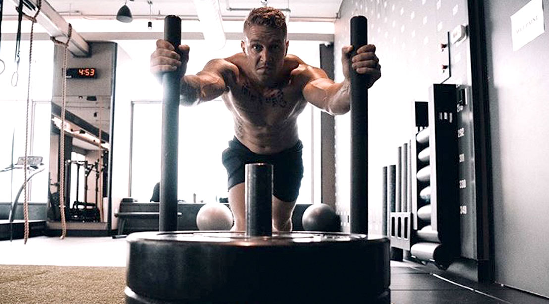 Army vet Erik Bartell working out in a gym performing a sled push exercise