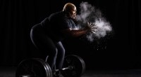 Black female powerlifter Tamara Walcott chaulking her hands before powerlifting a barbell